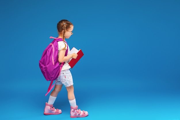 Happy smiling little girl with glasses and a book is going to school