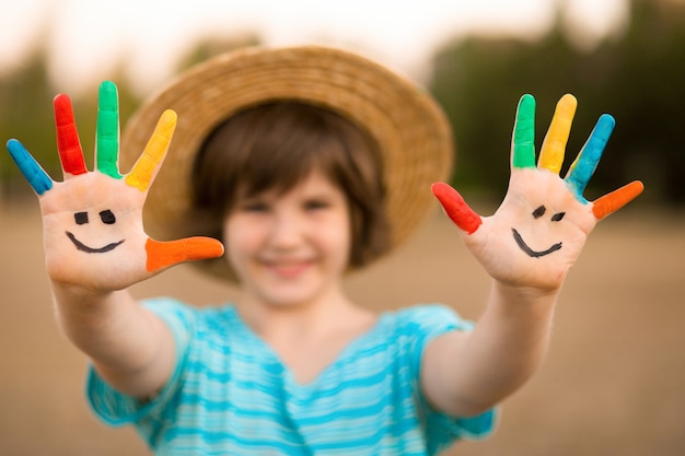 変な顔で描かれた手で幸せな笑顔の少女は夏の公園で屋外で遊ぶ手に焦点を当てる
