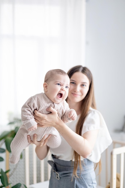 A happy smiling little newborn baby girl in her mother's arms in closeup focus at home in the sleeping nursery by the bed Mother's love