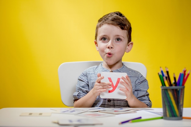 Happy smiling little preschool boy shows letters at home making homework at the morning before the school starts. English learning for kids.