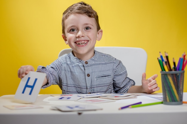 Il ragazzino prescolare sorridente felice mostra le lettere a casa che fanno i compiti la mattina prima dell'inizio della scuola. apprendimento dell'inglese per bambini.