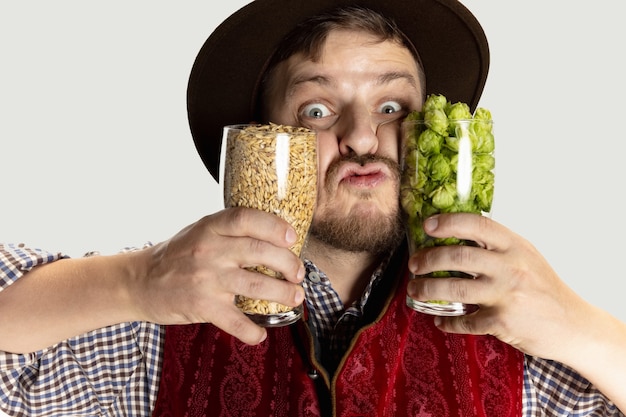 Sorridenti uomo vestito con il tradizionale costume austriaco o bavarese seduto a tavola con cibo festivo e birra isolate su sfondo rosso