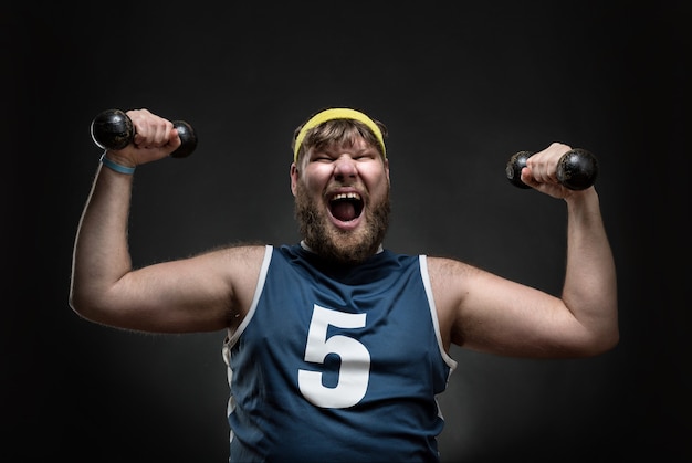 Happy smiling man with dumbbells in his both hands over grey