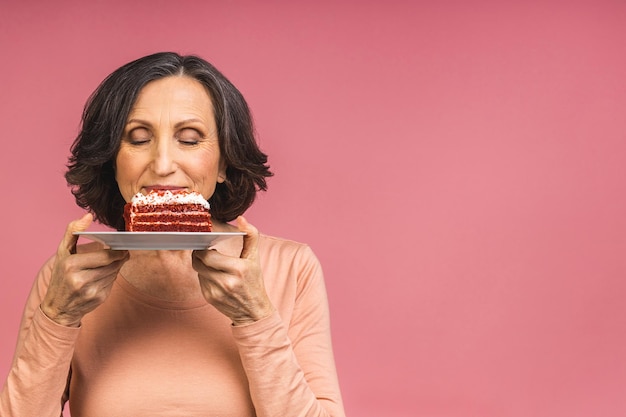 Photo happy smiling mature aged senior woman holding a birthday cake isolated over pink background.