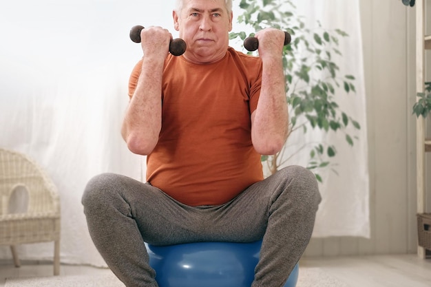 Happy smiling mature senior man doing exercises of gymnastics at home Concept of healthy lifestyle fitness recreation well being Elderly male exercising training stretching Old man working out