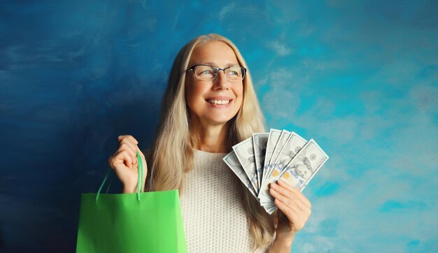 Happy smiling middle aged woman with shopping bags holding cash money in dollar bills in hands