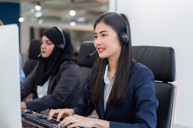 Счастливый улыбающийся оператор азиатских женщина агент по обслуживанию клиентов с гарнитурой работает на компьютере в колл-центр