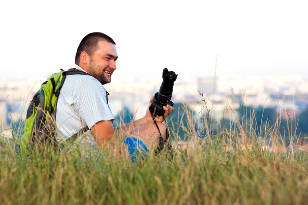 Happy smiling photographer sitting in grass in summer with a camera