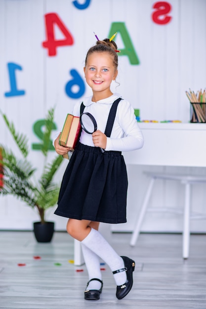 Happy smiling pupil at the desk. Child in the class room with pencils, books. Kid girl from primary school.