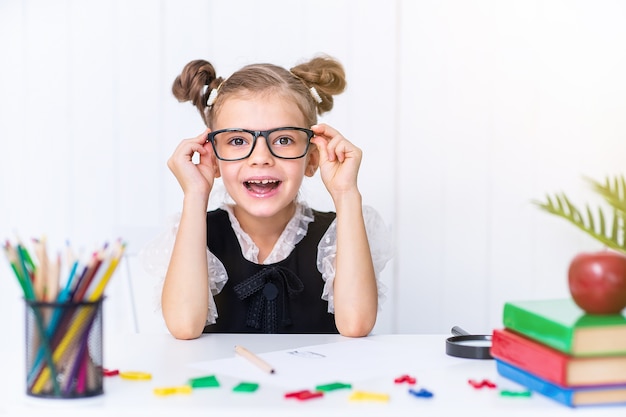 Happy smiling pupil at desk in classroom with pencils and books