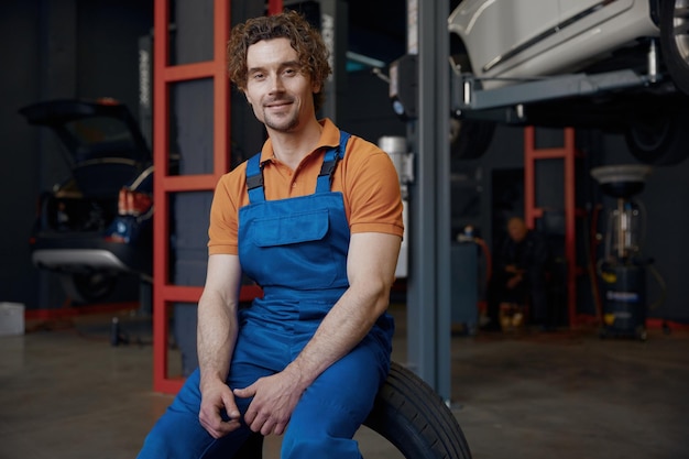 happy smiling relaxed male mechanic sitting on tire in garage car service