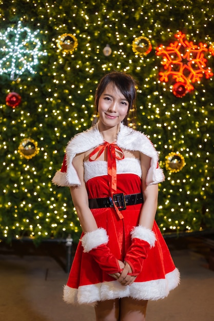 Happy smiling Santa girl is cute in red suit with christmas tree background 