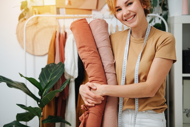 Sarta sorridente felice che abbraccia rotoli di tessuto sorriso visibile a metà faccia scaffali con vestiti sullo sfondo