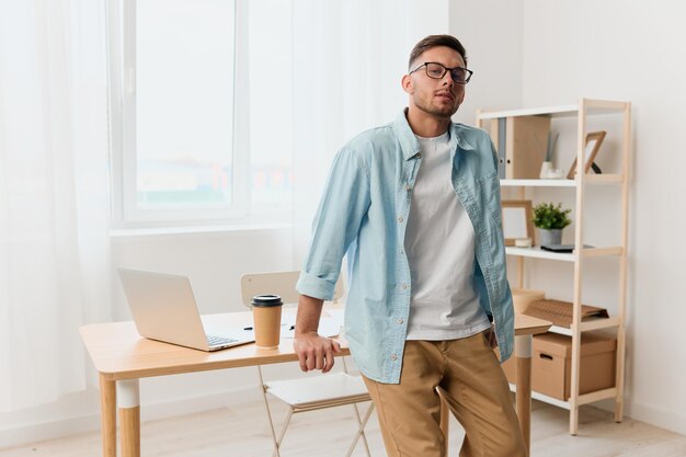 Happy smiling selfconfident handsome stylish young businessman\
in eyewear reclines on table looks at camera staying in office copy\
space for ad remote job technology and career profession\
concept