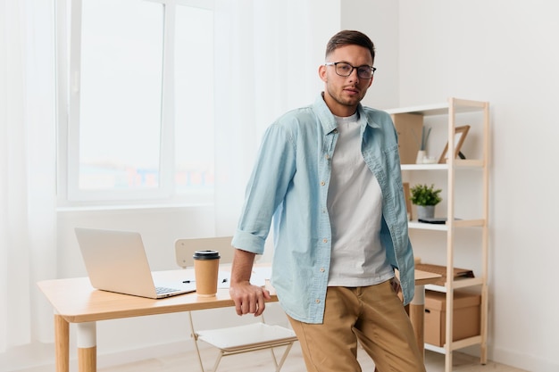 Happy smiling selfconfident handsome stylish young businessman\
in eyewear reclines on table looks at camera staying in office copy\
space for ad remote job technology and career profession\
concept