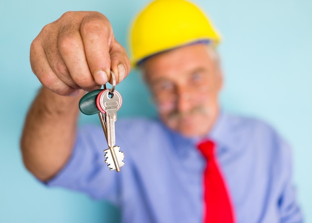 Счастливый улыбающийся старший архитектор, держащий ключи для готового нового дома