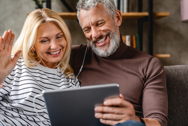 Coppia senior sorridente felice con computer tablet digitale con videochiamata a casa