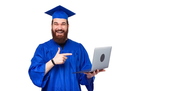 Счастливый улыбающийся студент человек, носящий синий холостяк, указывая на ноутбук