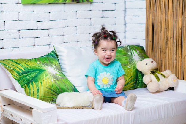 Счастливая улыбающаяся милая девочка сидит на диване с игрушкой медведя