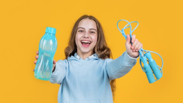 Happy smiling teen girl hold sport or fitness equipment of jumping rope and water bottle, refreshment.