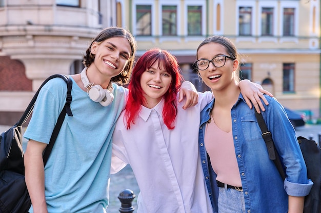 Happy smiling teenage friends hugging looking at camera outdoor on city street friendship community youth lifestyle leisure fun concept