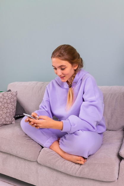 Happy smiling teenage girl with her smartphone browsing social newtwork communicating relaxed on a couch at home