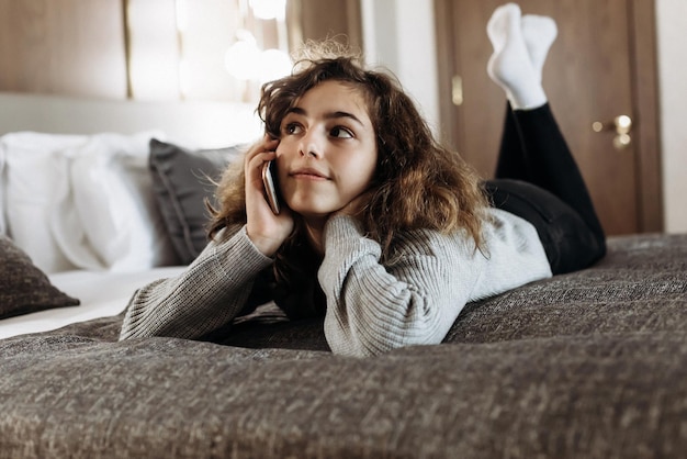 Happy smiling teenager girl talking by phone lying on the bed