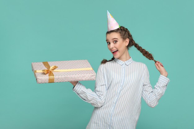 Happy smiling teenager in party cone holding present box being in festive mood