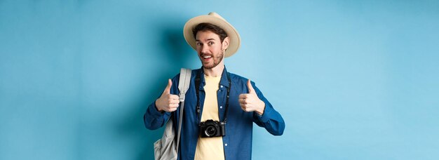 Happy smiling tourist say yes and show thumbs up going on summer vacation holding backpack and photo