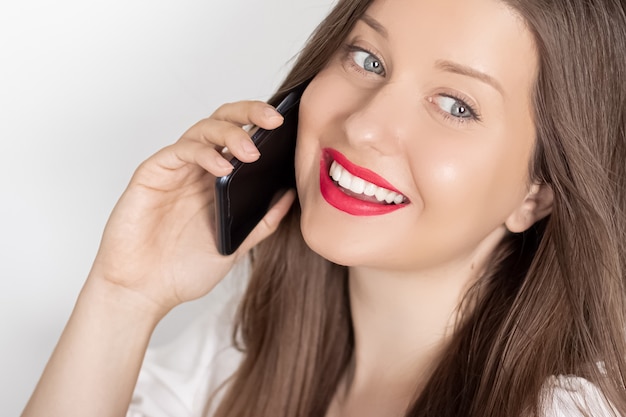 Donna sorridente felice che invita il ritratto dello smartphone sul concetto bianco della tecnologia e della comunicazione della gente del fondo