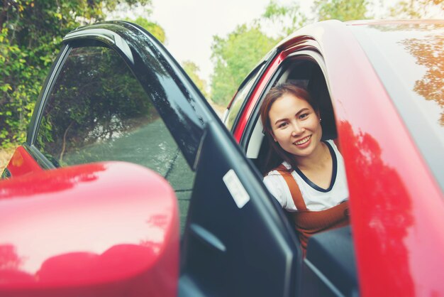 日光と赤い車の中で幸せな笑顔の女性