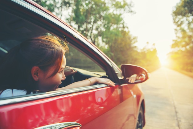 日光と赤い車の中で幸せな笑顔の女性