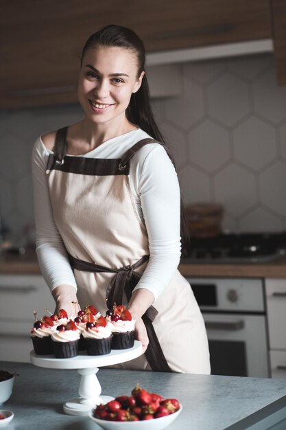 Photo happy smiling woman decorating tasty chocolte muffins with fresh fruits