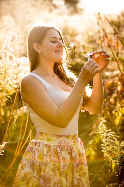 Happy smiling woman in dress looking at flower growing at field