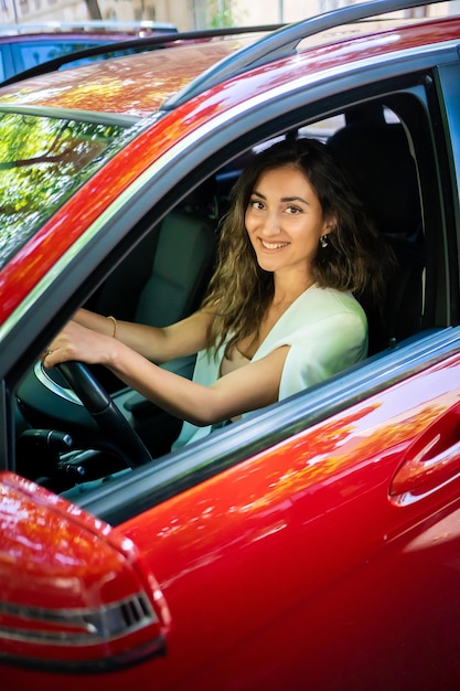 Happy smiling woman driver behind the wheel red car View through car window