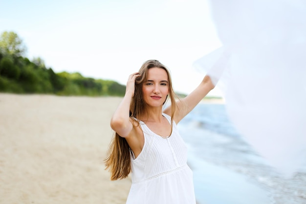 Photo happy smiling woman in free happiness bliss on ocean beach catching clouds. portrait of a multicultural female model in white summer dress enjoying nature during travel holidays vacation outdoors.