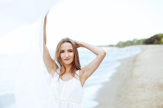 Happy smiling woman in free happiness bliss on ocean beach catching clouds. Portrait of a multicultural female model in white summer dress enjoying nature during travel holidays vacation outdoors