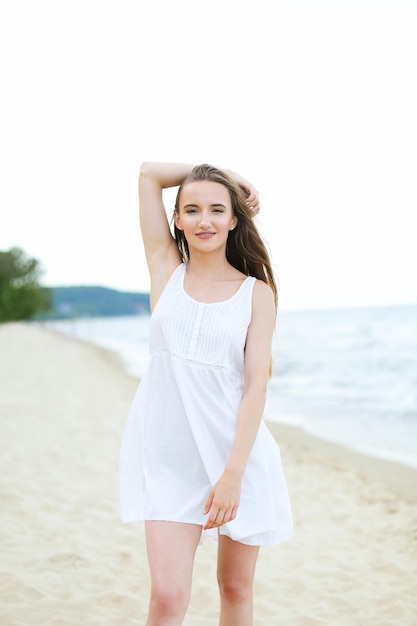 똑바로 서있는 바다 해변에서 무료 행복 행복에 행복 웃는 여자. 여행 휴가 야외에서 자연을 즐기는 흰색 여름 드레스에 다문화 여성 모델의 초상화