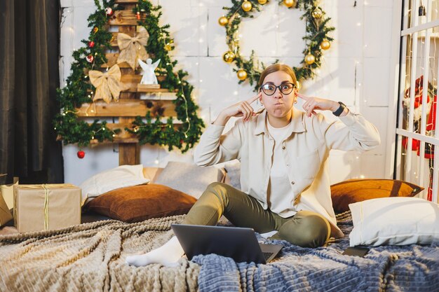 Foto felice donna sorridente con gli occhiali giace sul letto sullo sfondo delle decorazioni natalizie la donna è felice delle vacanze di natale atmosfera di capodanno a casa