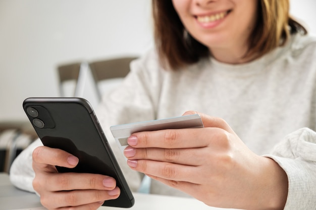 Happy smiling woman holding credit card and paying by mobile phone customer makes shopping online