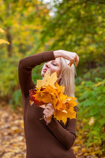 黄色いカエデの葉を手に持って幸せな笑顔の女性