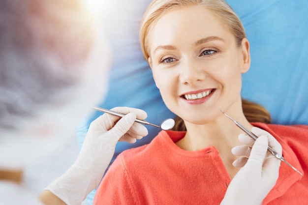 행복한 미소 짓는 여성이 치과 병원에서 치과의사에게 검사를 받고 있습니다. 건강한 치아와 의학 구강학 개념