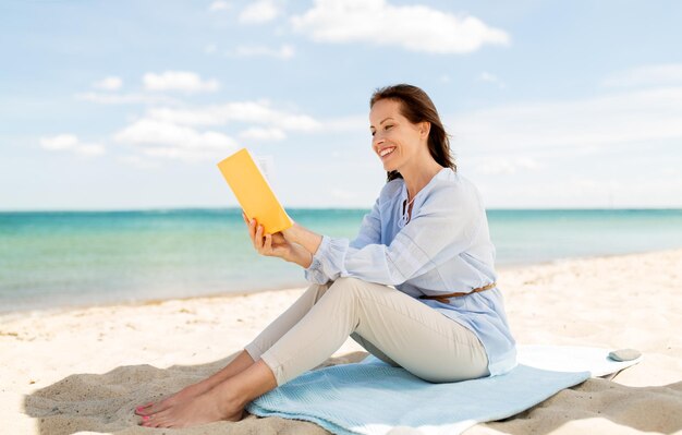 Foto donna sorridente felice che legge un libro sulla spiaggia estiva