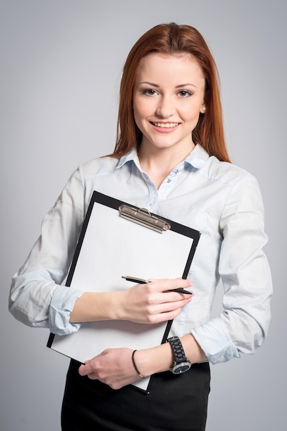 Happy smiling woman in strict clothes and glasses holding a clipboard on grey