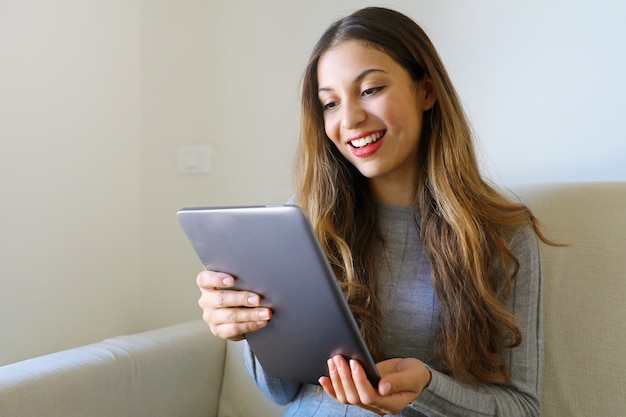 Happy smiling womanusing tablet sitting on sofa at home