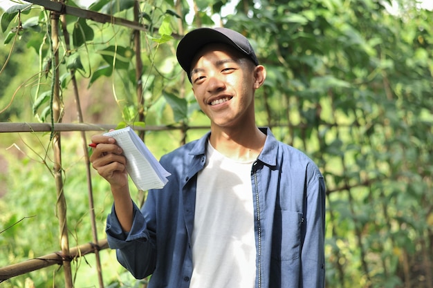 Happy of smiling young Asian farmer male holding the notebook on green garden, on location.