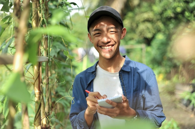 Happy of smiling young Asian farmer male holding the notebook on green garden, on location.