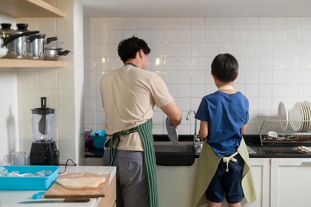 幸せな笑みを浮かべて若いアジアの父と息子が自宅のキッチンで皿洗い