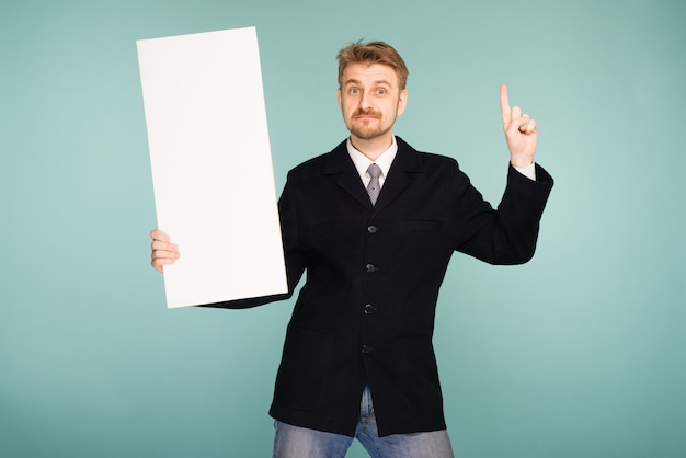 Happy smiling young business man showing blank signboard, on blue 