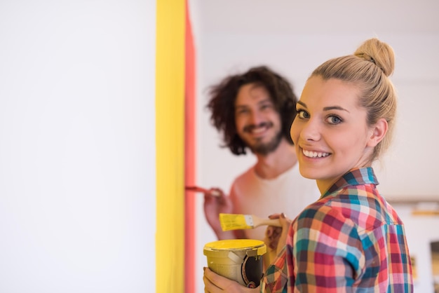 Photo happy smiling young couple painting interior wall of new house